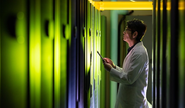 Foto ingeniero asiático con un delantal usando una tableta digital mientras inspecciona la sala de servidores de computadoras. concepto de gestión y mantenimiento del servidor de bases de datos
