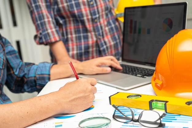 Foto el ingeniero asiático y el equipo asociado aprenden y hablan con el gráfico del plano del proyecto del plan de la casa y el casco amarillo y las herramientas de construcción de ingeniería en el trabajo de la mesa