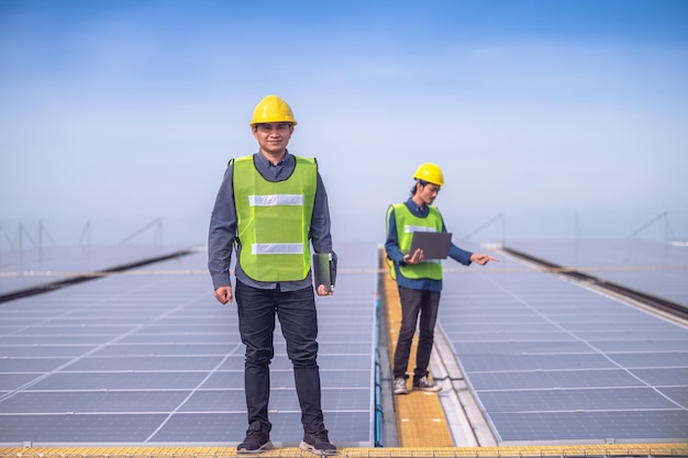 Ingeniero asiático del equipo parado en la fábrica de la azotea y comprobando la energía de las células solares de energía solar mediante tecnología de tabletas