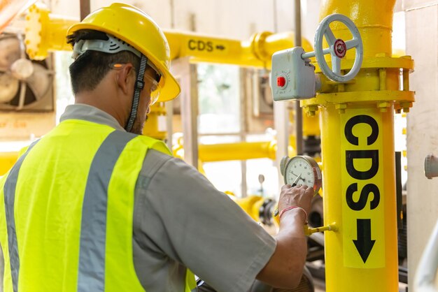 Ingeniero asiático con gafas trabajando en el mantenimiento de la sala de calderas comprobando los datos técnicos del equipo del sistema de calefacciónGente tailandesa