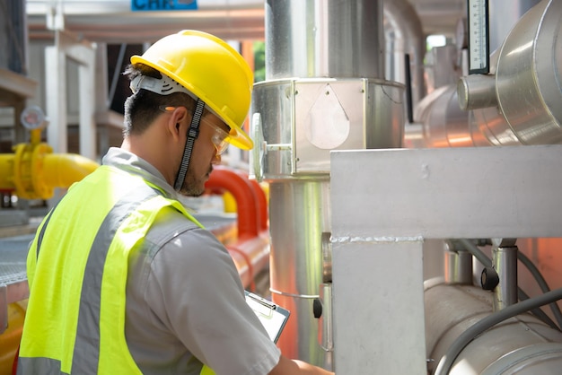 Ingeniero asiático con gafas trabajando en el mantenimiento de la sala de calderas comprobando los datos técnicos del equipo del sistema de calefacciónGente tailandesa