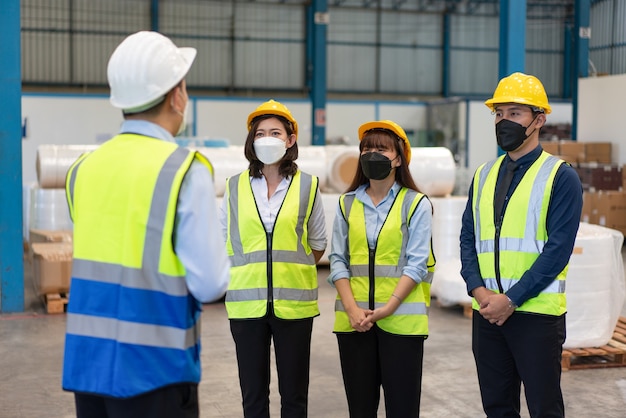 El ingeniero asiático del grupo usa una máscara que protege con una reunión permanente de seguridad del casco antes de trabajar en la fábrica.