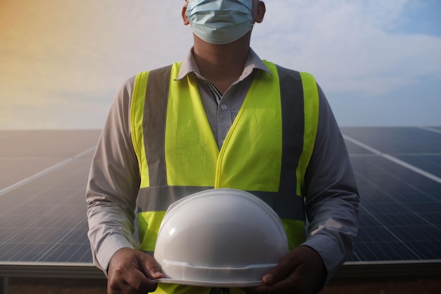 Ingeniero asiático joven que sostiene un casco blanco contra un fondo