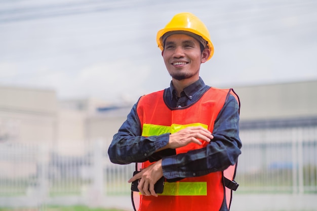 Ingeniero asiático parado al aire libre en la construcción del sitio publicando confianza en la construcción del ingeniero feliz éxito en el trabajo con la planificación de objetivos