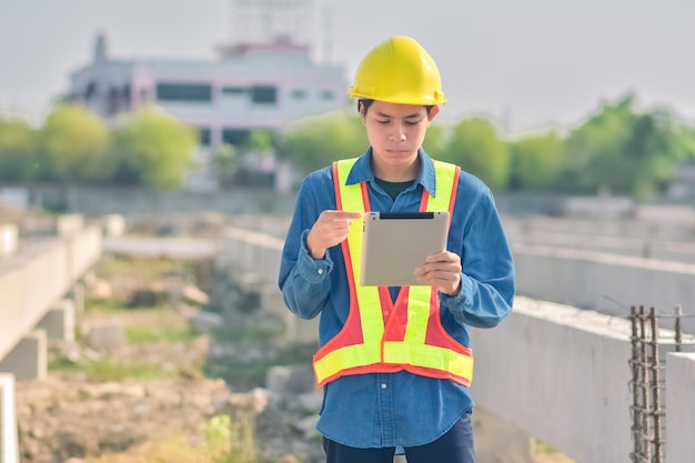 Ingeniero asiático parado al aire libre en la construcción del sitio publicando construcción de ingenieros confiados