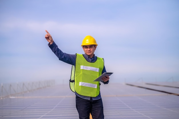 Ingeniero asiático de pie en la fábrica de la azotea y comprobando la energía de las células solares de energía solar mediante tecnología de tabletas