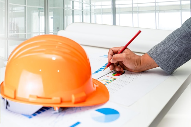 Ingeniero asiático con plano arquitectónico de proyecto de casa y casco amarillo y herramientas de construcción de ingeniería