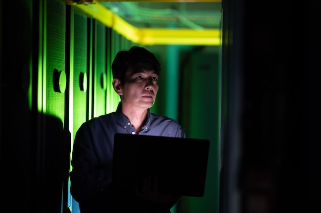 Ingeniero asiático que usa una computadora portátil mientras inspecciona la sala de servidores de computadoras. concepto de gestión y mantenimiento del servidor de bases de datos