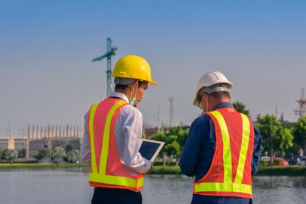 Ingeniero asiático y trabajador capataz con panel táctil discuten el plan de trabajo para el sitio de construcción de edificios al aire libre