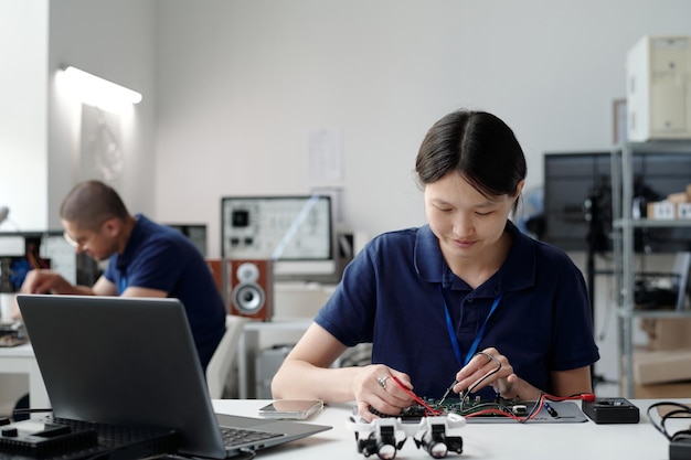 Ingeniero asiático trabajando en un dispositivo electrónico en un laboratorio moderno
