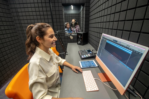 Ingeniero de audio alegre sentado en el escritorio mirando la pantalla digital durante la grabación de música