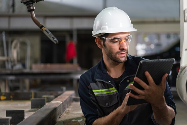 Ingeniero de automatización masculino con control de tableta máquina de soldadura de brazo robótico en fábrica industrial