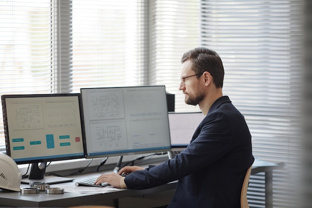 Ingeniero barbudo usando una computadora con planos en la pantalla en la oficina