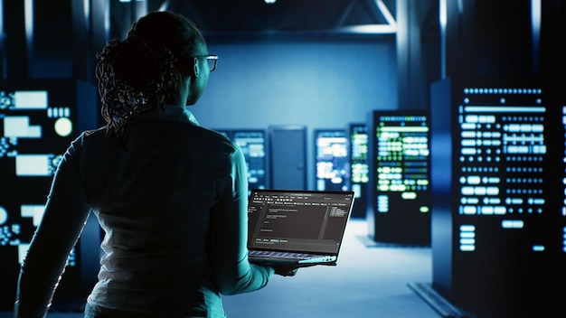 Ingeniero caminando en una sala de servidores que alberga una infraestructura avanzada que almacena conjuntos de datos masivos. Trabajador ejecuta código en una tableta para actualizar las plataformas del centro de datos que realizan operaciones computacionales complejas