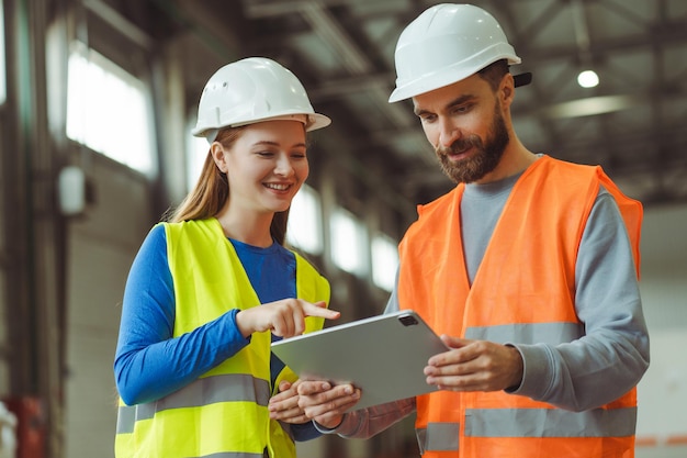 Ingeniero capataz de fábrica y trabajadora que usa cascos blancos protectores usando una tableta digital