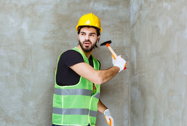 Ingeniero en casco amarillo y guantes industriales golpeando el muro de hormigón con un hacha
