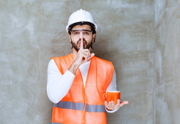 Ingeniero con casco blanco sosteniendo una taza naranja y pidiendo una llamada.