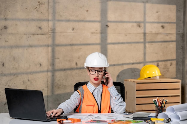 Foto ingeniero en casco y chaleco trabajador civil inteligente joven linda chica rubia en llamada telefónica