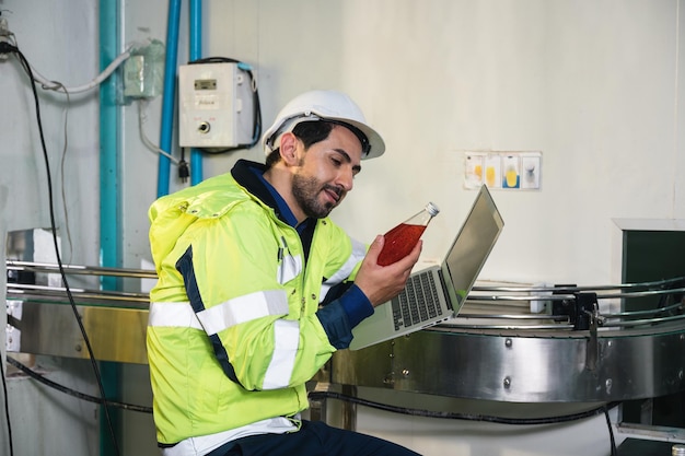 Foto ingeniero caucásico con uniforme de seguridad comprobando e informando la calidad de una fruta embotellada en la cinta transportadora en la planta de procesamiento