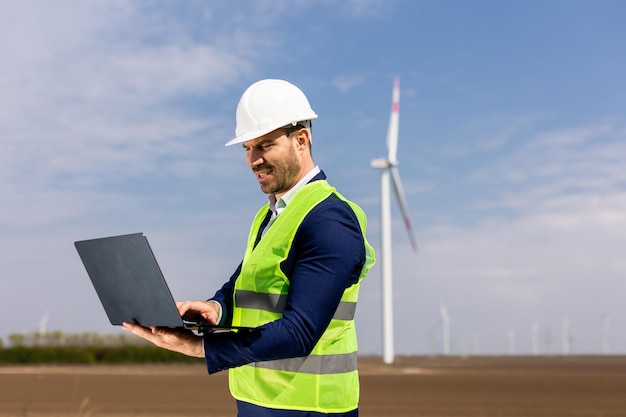 Ingeniero en chaleco de alta visibilidad analizando datos en la computadora portátil en el parque eólico durante el día IA generativa