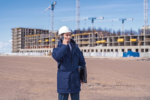 Un ingeniero civil con un casco blanco está hablando por teléfono en la construcción.