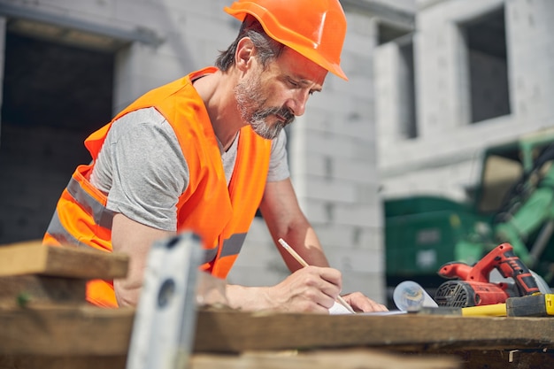 Ingeniero civil profesional serio con un lápiz en la mano mirando el plano de planta