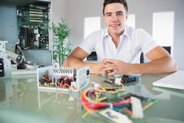 Ingeniero en computación atractivo sentado en el escritorio sonriendo a la cámara