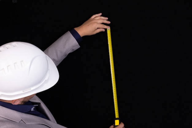 Ingeniero de construcción empresario en un casco blanco mide la distancia con una cinta métrica