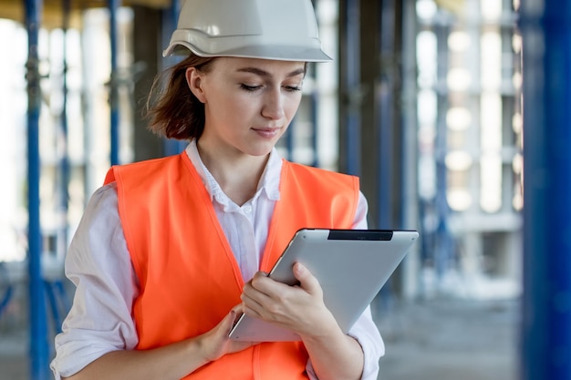 Ingeniero de construcción femenino. Arquitecto con una tableta en un sitio de construcción. Mujer joven mirando, lugar de construcción en segundo plano. Concepto de construcción.