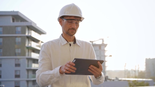 El ingeniero de construcción o arquitecto que lleva una camisa blanca y un sombrero duro está usando una tableta digital