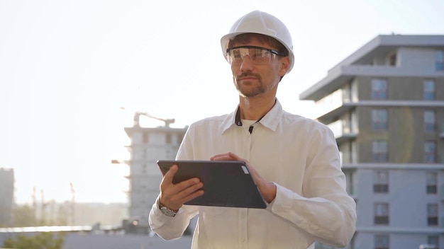 El ingeniero de construcción o arquitecto que lleva una camisa blanca y un sombrero duro está usando una tableta digital