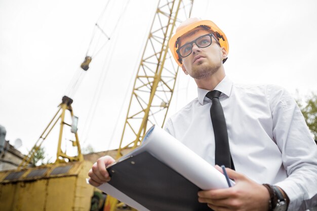 Ingeniero constructor en un casco tiene dibujos en el sitio de construcción