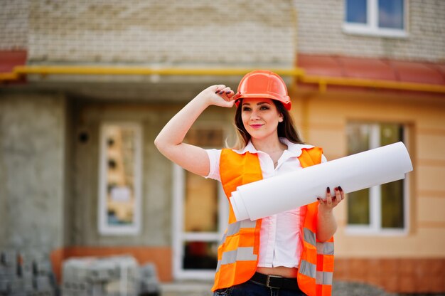 Ingeniero constructor mujer en chaleco uniforme y casco protector naranja mantenga papel comercial contra nuevo edificio