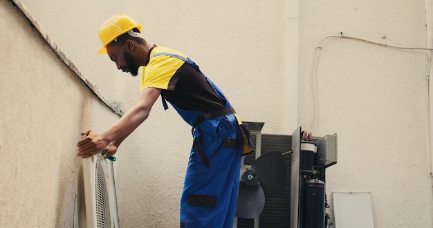 Ingeniero desmantelando el acondicionador de aire para limpiar los desechos sueltos acumulados en el interior. Especialista capaz que se prepara para limpiar el cuerpo del sistema HVAC y el panel de control con una herramienta de cepillo para polvo para eliminar la suciedad suelta