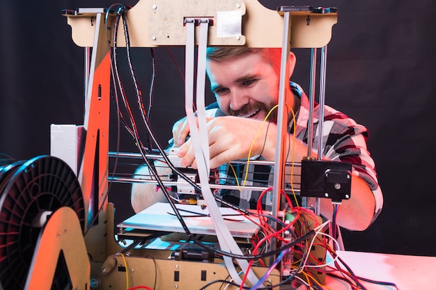 Ingeniero diseñador masculino joven que usa una impresora en el laboratorio y estudia un concepto de prototipo, tecnología e innovación de producto.