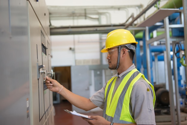 Ingeniero eléctrico asiático con portapapeles para verificar y monitorear el sistema eléctrico en la sala de controlTécnico tailandia personas trabajando