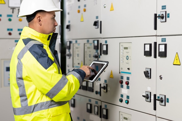 Ingeniero eléctrico de hombre asiático mantenga el sistema eléctrico de monitoreo de tableta en técnico de sala de control