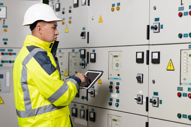 Ingeniero eléctrico de hombre asiático mantenga el sistema eléctrico de monitoreo de tableta en técnico de sala de control