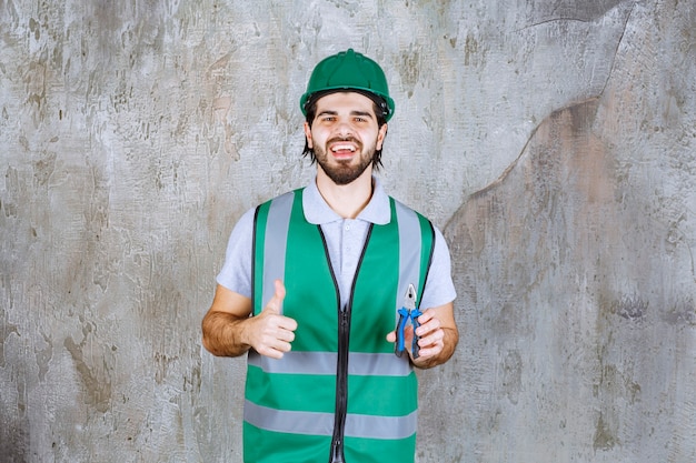 Ingeniero en engranaje amarillo y casco sosteniendo alicates y mostrando el pulgar hacia arriba