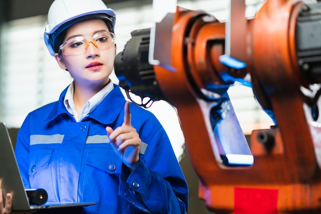 Ingeniero especialista asiático femenino y mantenimiento técnico inspeccionar el sistema de brazo de robot de relé con computadora portátil para controlar la calidad operar proceso trabajo industria pesada 40 fabricación fábrica inteligente