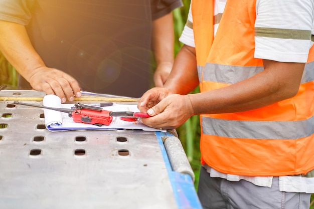 Un ingeniero está usando un teléfono celular para verificar precios y reuniones de trabajo con trabajadores en el sitio de construcción con bengalas solares