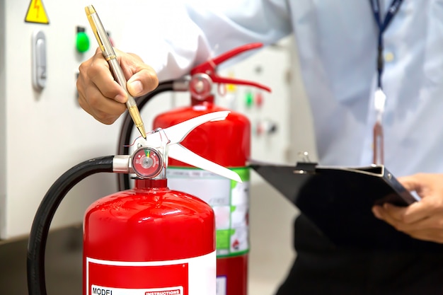 El ingeniero está verificando e inspeccionando un extintor de incendios en la sala de control de incendios por seguridad y prevención.