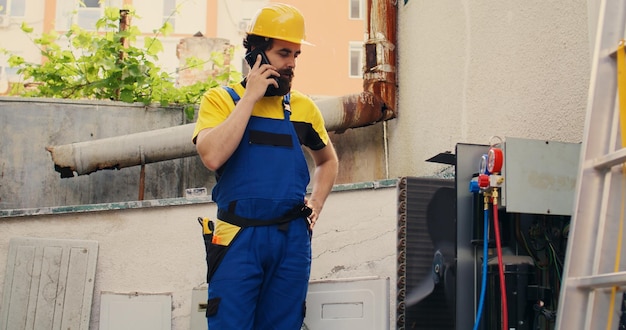 Ingeniero experto hablando por teléfono con el dueño de la casa después de terminar las reparaciones del sistema hvac. Reparador experto que llama al cliente para informarle sobre las capas acumuladas de suciedad encontradas en la unidad de aire acondicionado