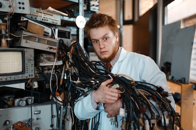 El ingeniero extraño sostiene un montón de cables con diferentes enchufes en el laboratorio.