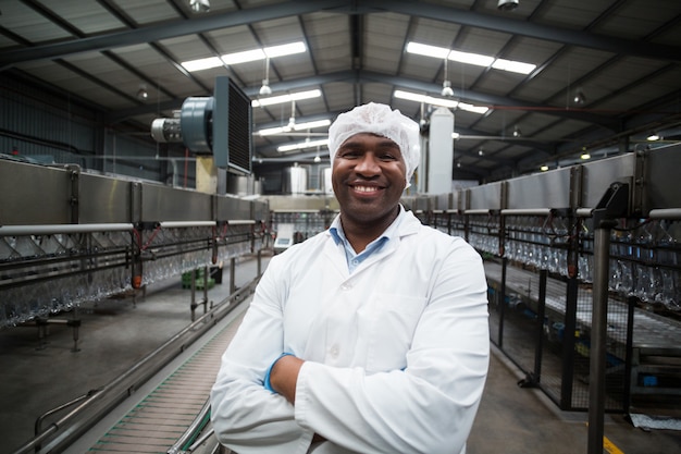 Ingeniero de fábrica sonriente de pie con los brazos cruzados en la fábrica de botellas