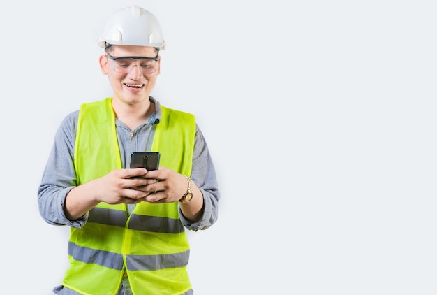 Un ingeniero guapo con un teléfono aislado un ingeniero constructor alegre enviando mensajes de texto en un fondo aislado un joven ingeniero con chaleco y casco usando un teléfono móvil