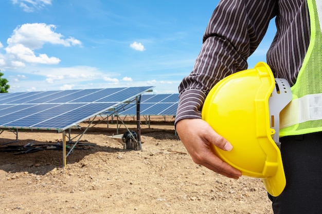 Ingeniero de hombre de negocios joven mantenga casco amarillo en el fondo del sitio de construcción de la planta de energía del panel solar