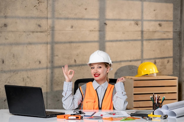 Ingeniero inteligente joven linda chica rubia trabajadora civil en casco y chaleco feliz por el nuevo edificio