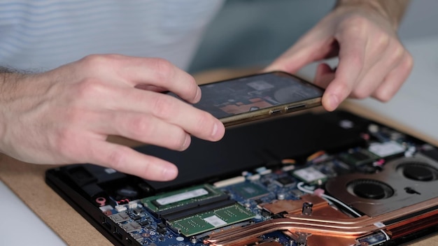 Ingeniero irreconocible toma fotografías de la placa base de la computadora portátil en un teléfono inteligente