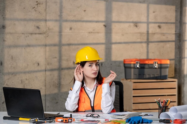 Ingeniero joven linda chica morena inteligente trabajador civil en casco y chaleco escuchando a escondidas